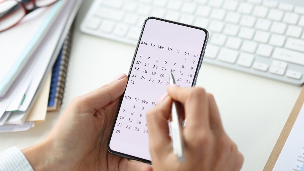 imagine cu o fată care are un calendar pe telefon în mână și un pix